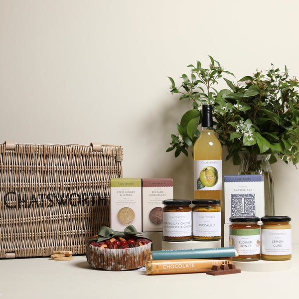 A wicker hamper basket with biscuits, lemonade, a fruit cake, chocolates, honey and chutney.